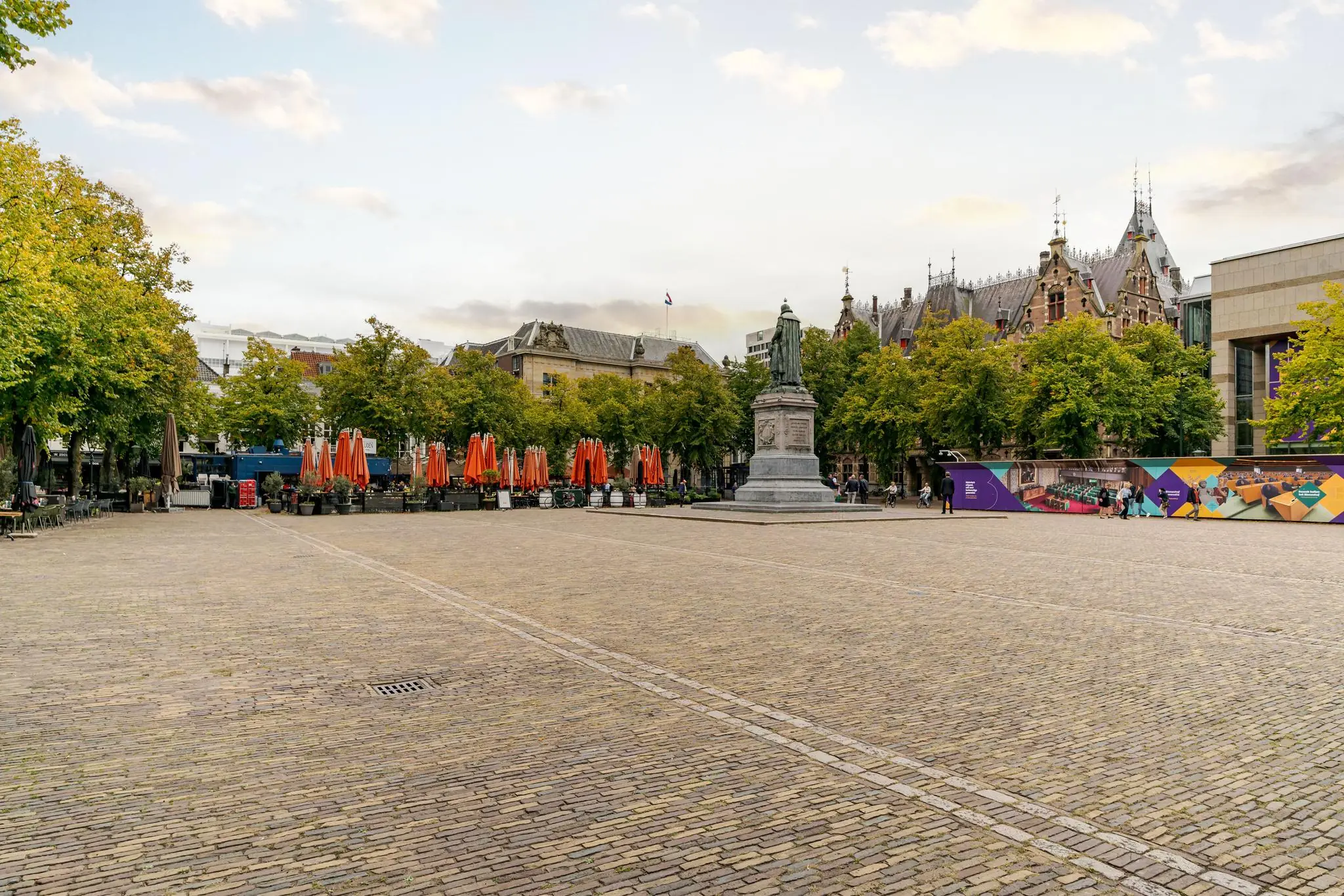 Plein met standbeeld en terrasparasols op het Lange Voorhout in Den Haag.